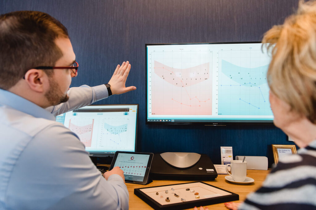 Hörakustiker erklärt Kundin ein Audiogramm am großen Bildschirm.