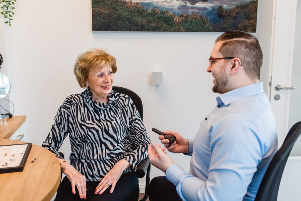 Lachende Kundin im Beratungsgespräch mit einem Hörakustiker.