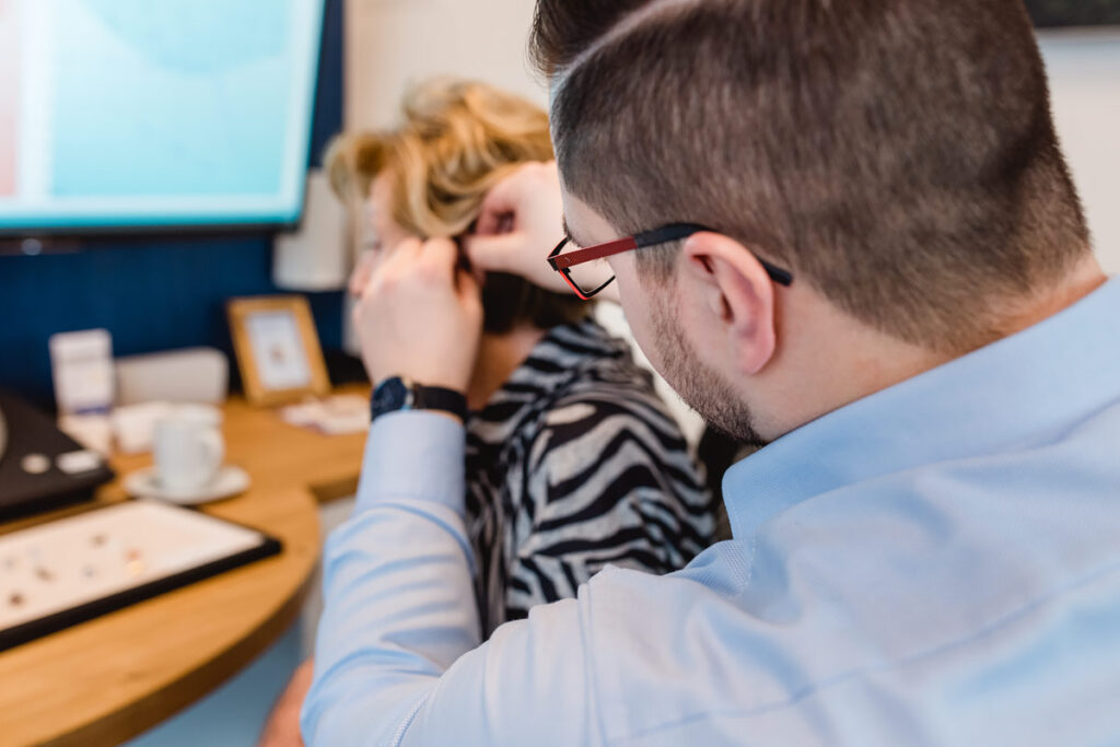 Hörakustiker setzt ein Hörgerät präzise hinter das Ohr einer Kundin.