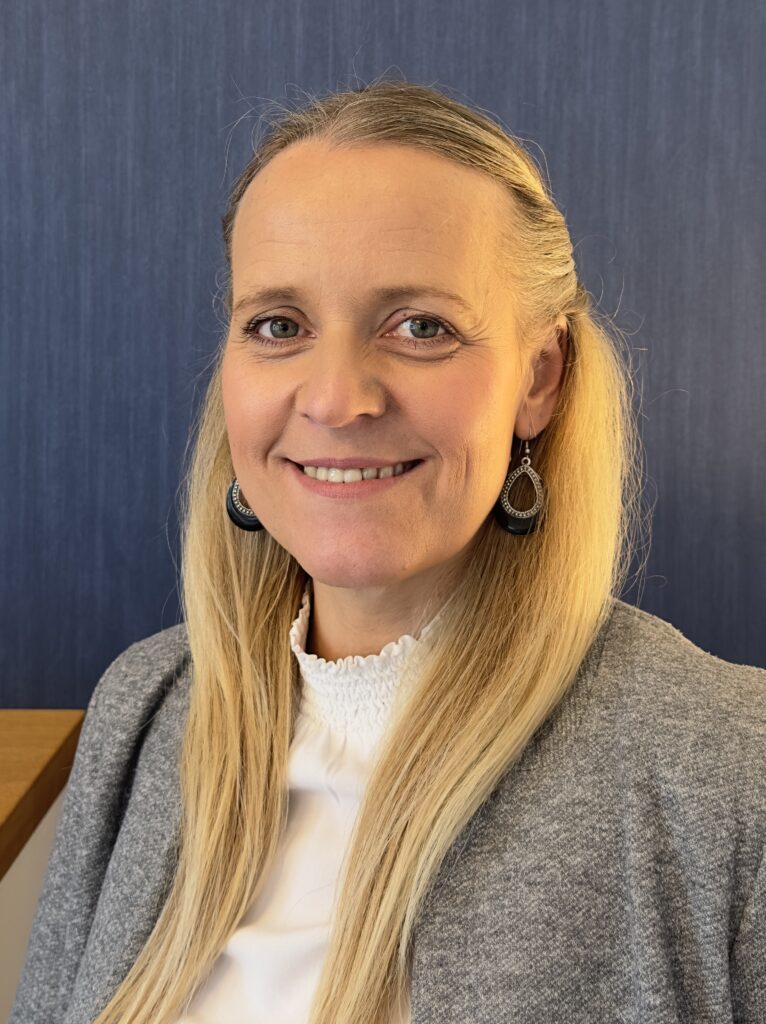 Eine Frau mit blonden Haaren lächelt freundlich in die Kamera.